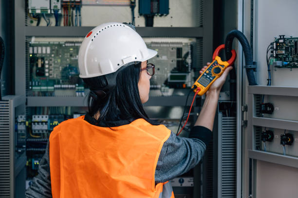 Young female maintenance engineer testing voltage with digital multimeter Young woman industrial service electrician engineer wearing protective vest and white technician helmet testing and checking fridge electric voltage with digital multimeter electric measurement instrument a control panel fuse box in boiler energy control room of modern thermal or nuclear power plant electric energy station. xxxl size taken with canon 5d mIV electrician multimeter stock pictures, royalty-free photos & images