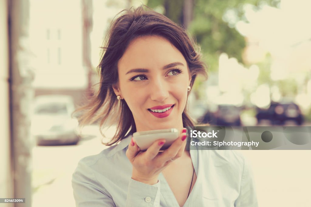 Woman using a smart phone voice recognition function online walking on a city street Woman using a smart phone voice recognition function online walking on a city street on a summer day Voice Stock Photo