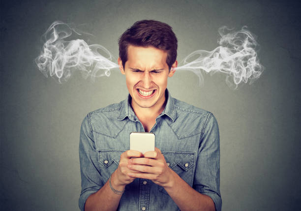 uomo arrabbiato frustrato che legge un messaggio di testo sul suo smartphone che soffia vapore che esce dalle orecchie - frustrazione foto e immagini stock