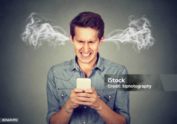 Frustrated Angry Man Reading A Text Message On His Smartphone Blowing Steam Coming Out Of Ears Stock Photo - Download Image Now