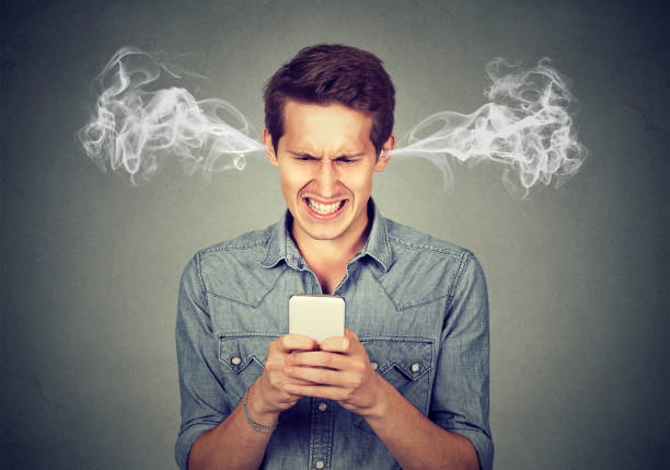 frustrated angry man reading a text message on his smartphone blowing steam coming out of ears - frustração imagens e fotografias de stock