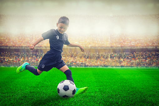asian soccer kid kicking football in the stadium
