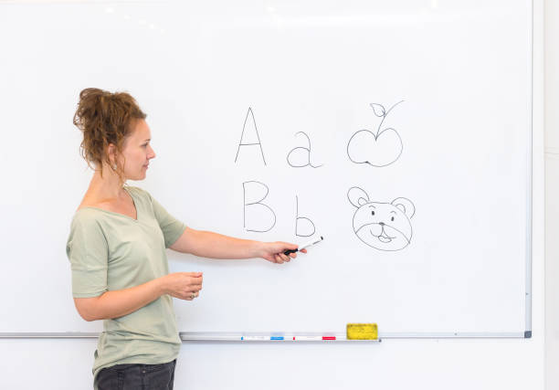 teacher woman teaches the letters on whiteboard in the classroom - blackboard teaching preschool alphabet imagens e fotografias de stock