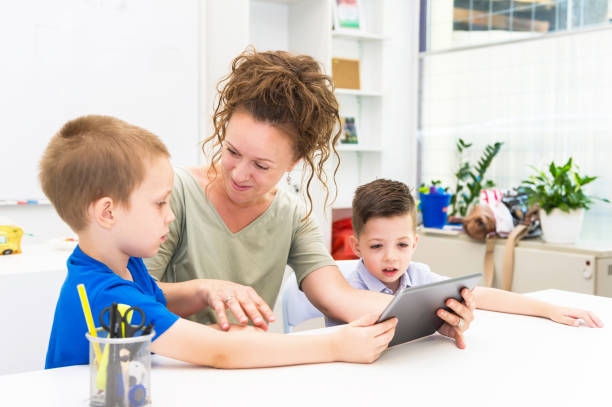 istock teacher woman using tablet computer with two preschooler boy in a classroom 824637418