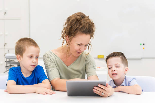 istock teacher woman using tablet computer with two preschooler boy in a classroom 824637470