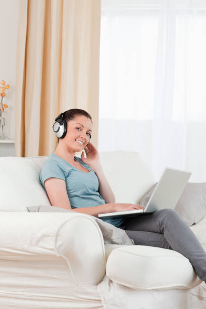 istock Charming woman with headphones relaxing with her laptop while sitting on a sofa 824638244