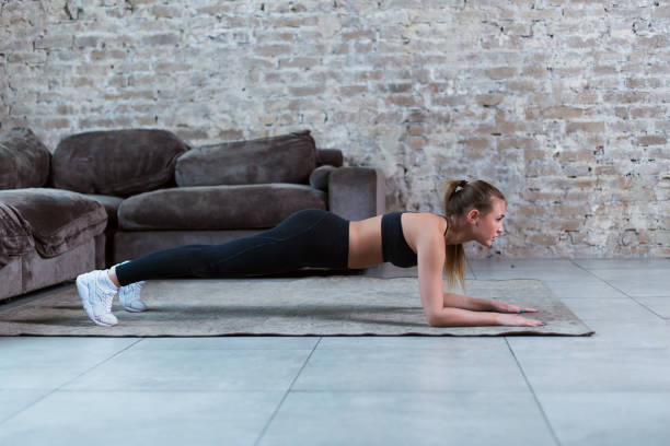 istock Slim young brunette wearing black gym clothing doing abdominal bridge or front plank exercise in loft apartment. 824638734