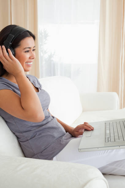 istock charming woman sitting on sofa with notebook and earphones 824663058