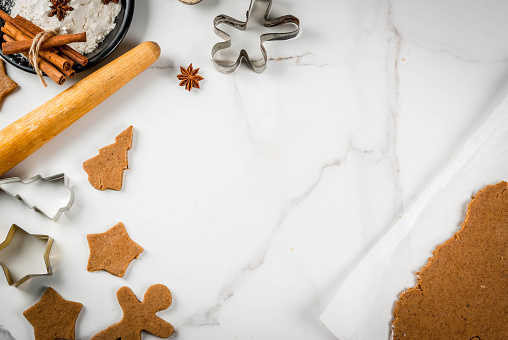 Christmas baking. Ginger dough for gingerbread, gingerbread men, stars, Christmas trees, rolling pin, spices (cinnamon and anise), flour. On the home kitchen white marble table. Copy space