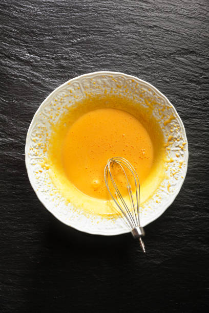 istock Whipped egg yolks in a white bowl and a top from an electric mixer with a black stone table 824674012