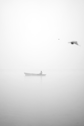 India Varanasi - January 30, 2016: In a very hazy morning, the Ganges River ferry and its boatman. Ganges are considered to be the holy river of India, attracting millions of pilgrims from India and around the world.