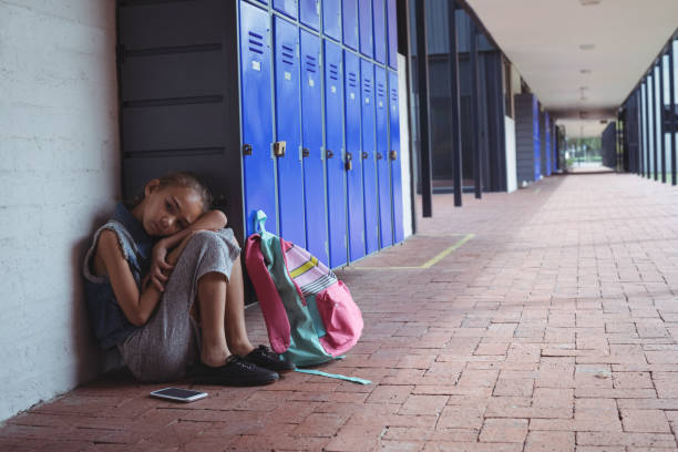 istock Full length of elementary schoolgirl resting by lockers 824696902