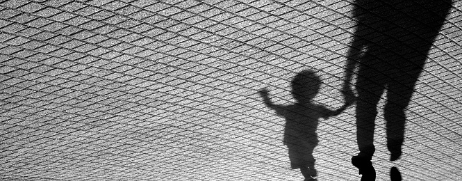 Blurry shadow of a joyful toddler boy walking hand in hand with his father