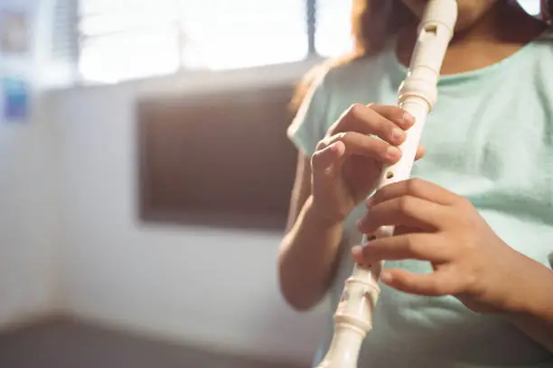 Mid section of girl playing flute in classroom at music school
