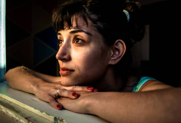 istock Young woman model posing leaning on the window with the sun lighting up his face. Wide angle lens, high contrast, selective focus. 824722716