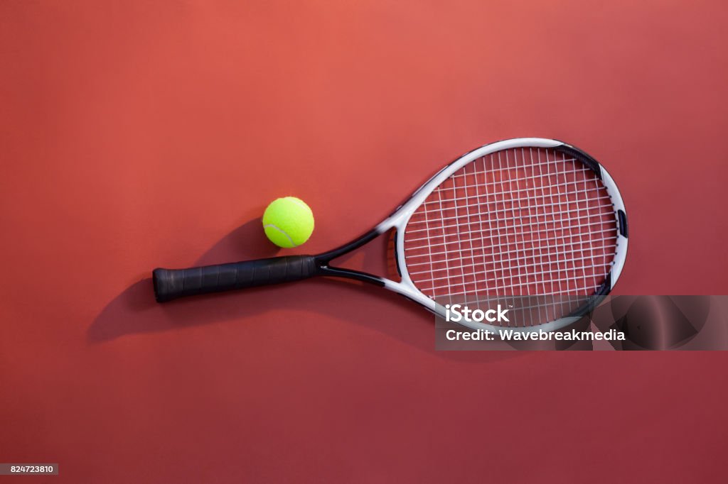 Overhead view of fluorescent yellow tennis ball on racket Overhead view of fluorescent yellow tennis ball on racket over maroon background Sphere Stock Photo