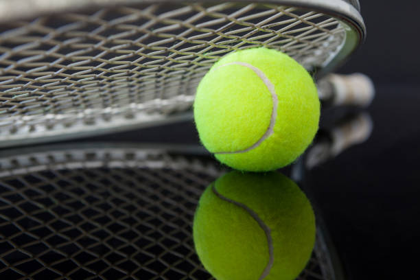 Close up of tennis racket on ball with reflection against black background