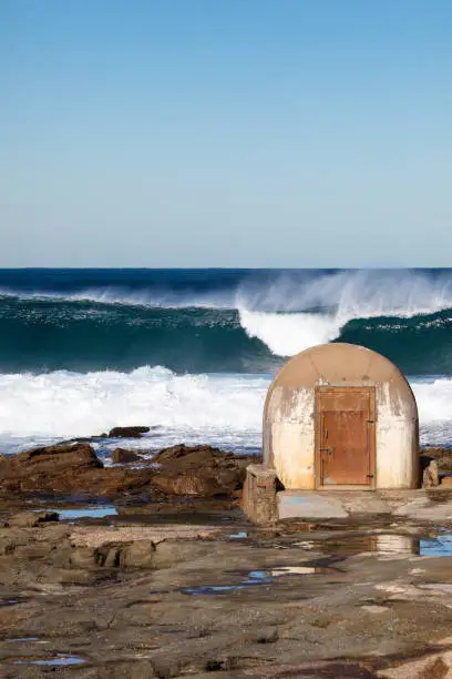 Large surf breaking beyond the pumphouse at the Cowrie Hole - Newcastle Australia. This pumphouse is a local landmark and delivers water to the adjacent Newcastle ocean baths.