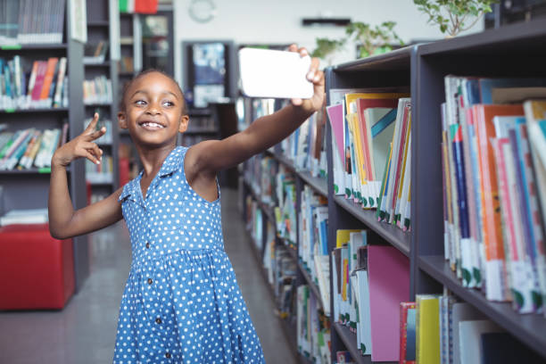 istock Smiling girl taking selfie by bookshelf in library 824750588