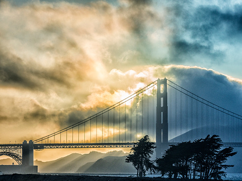Cropped, stormy, cloudy sunset view of the distant Golden Gate Bridge which crosses over the San Francisco Bay connecting the city of San Francisco, California and Marin County, California.