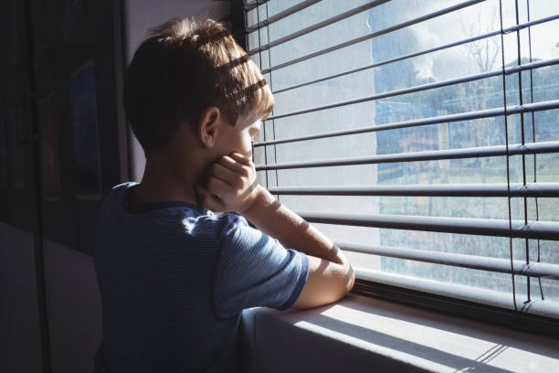 istock Boy looking through window glass of school 824763106