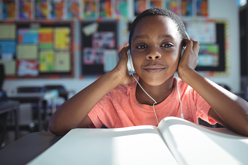 Portrait of boy listening music with headphones at desk in classroom