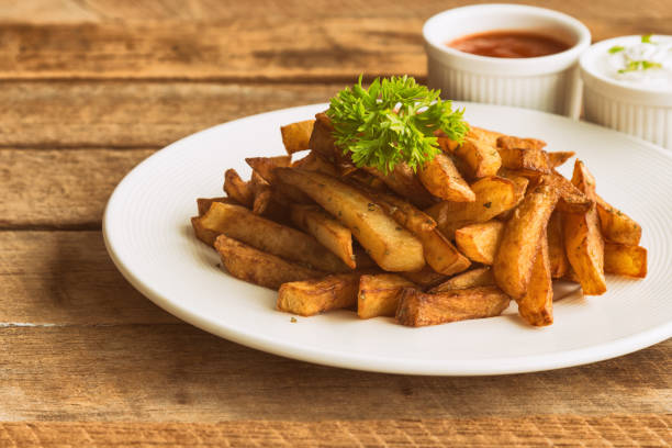 homemade french fries serve with ketchup and sour cream or mayonnaise. golden brown crispy french fries sprinkle with salt and oregano on white plate for snack or appetizer.french fries on wood table. - oregano freshness herb brown imagens e fotografias de stock