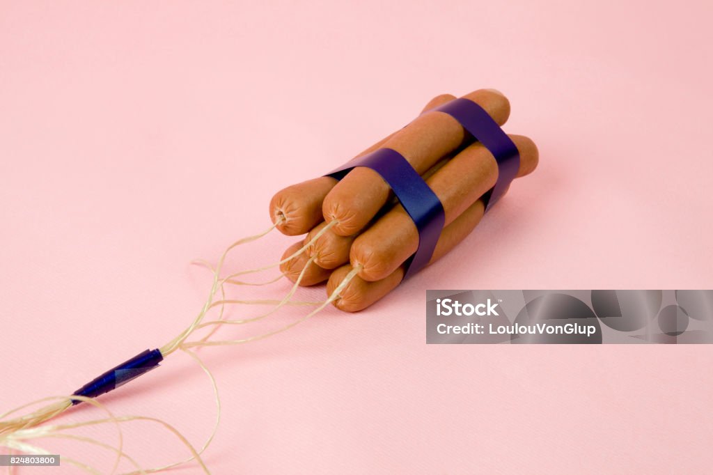 dynamite sausages pink sticks of dynamite are replaced by industrial sausages. Photographic composition funny and offbeat on a vibrant pink studio background. Fun, minimal and surreal color still life photography Humor Stock Photo