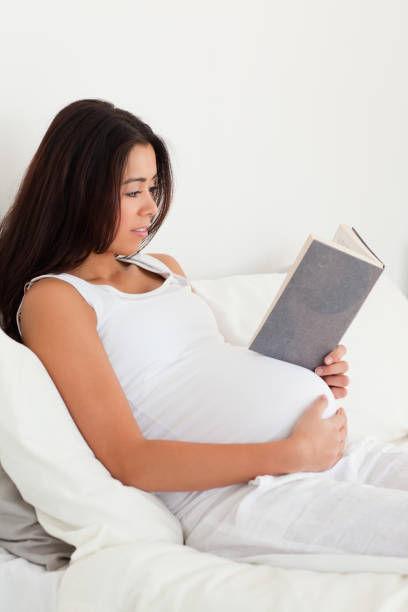 istock Charming pregnant woman reading a book while lying on a bed 824817084