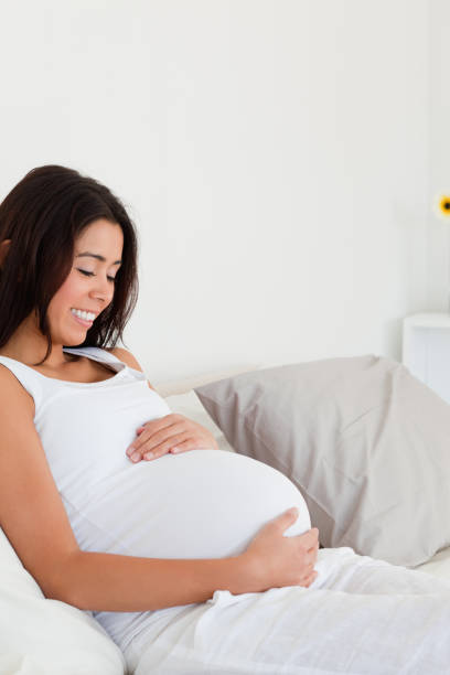 istock Gorgeous pregnant woman touching her belly while lying on a bed 824832714