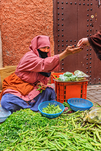 Morrocan woman selling vegetables on street market near Djemaa el Fna square, Marrakech, Morocco. Djemaa el Fna is a heart of Marrakesh's medina quarter.