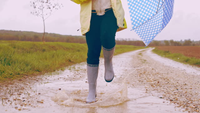 SLO MO Child with umbrella skipping through a puddle