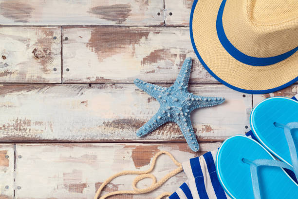 Summer vacation background with flip flops, starfish and hat on wooden board. View from above