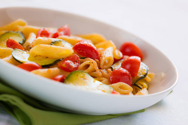Closeup of traditional italian penne pasta with zucchini and cherry tomatoes seasoned with oil and black pepper over a green napkin