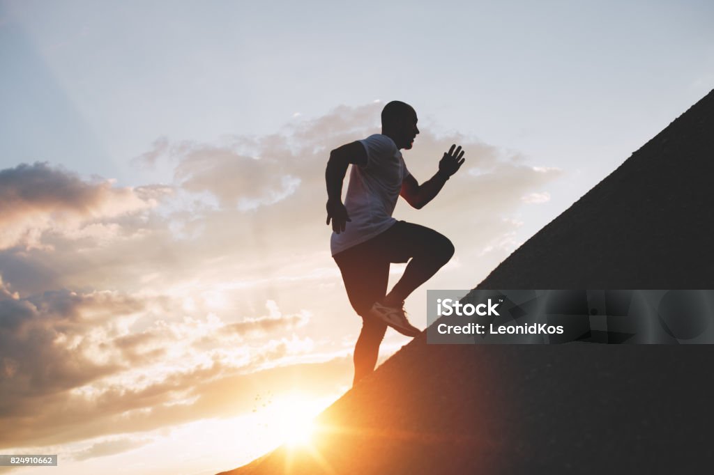 Male runner trains in an ascent to a mountain. Athlete runs through the mountains and hills at sunset Active Lifestyle Stock Photo