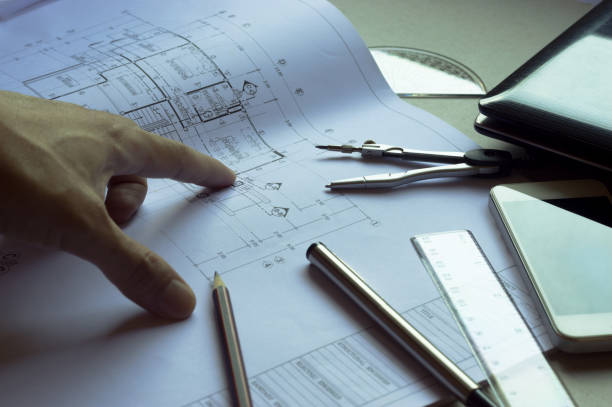 istock Divider, pencil, pen, ruler, glasses and smartphone and blueprint on table top.Table top view of Engineers table at office workplace.selective focus.Man hand pointing blueprint. 824913392