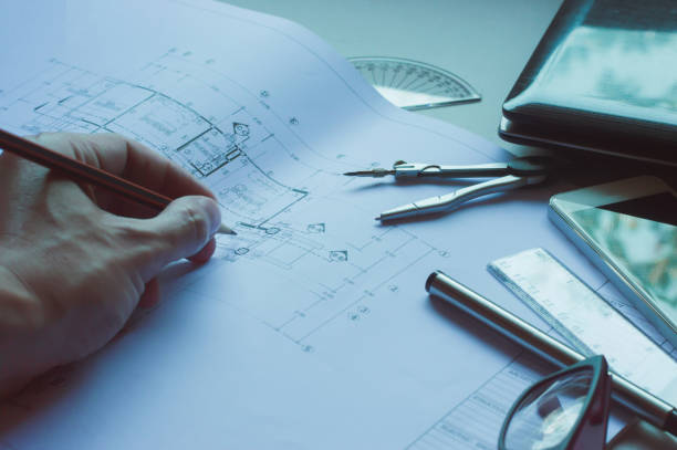 istock Divider, pencil, pen, ruler, glasses and smartphone and blueprint on table top.Table top view of Engineers table at office workplace.selective focus.Man hand editing blueprint. 824913670