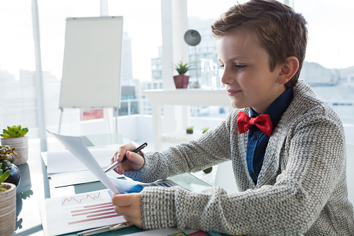 Boy as business executive verifying document in office