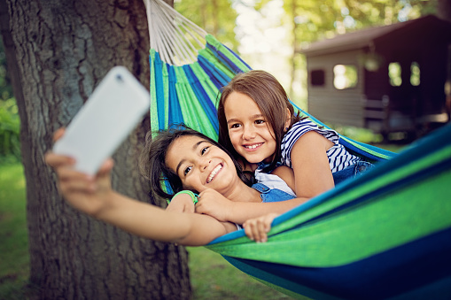Two sisters are lying down in the hammock and taking selfie/video call