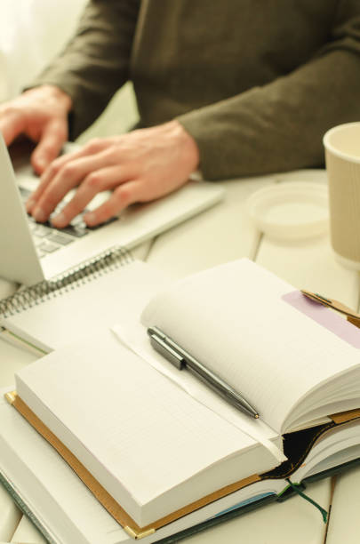istock Open notepad with black pen on work-table. Paper cup of coffee, office stuff, laptop and working man on background 824924350