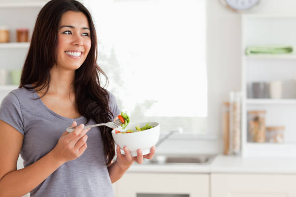istock Attractive woman enjoying a bowl of salad while standing 824925558