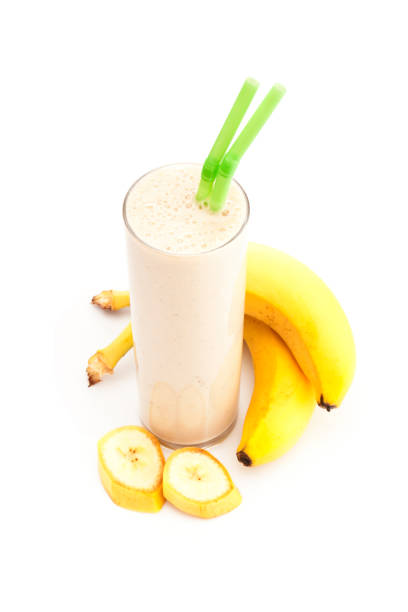 High angle view of a banana smoothie glass shot on white background. A colored drinking straw is in the glass and some banana fruit pieces are beside the glass. Predominant colors are yellow and white. DSRL studio photo taken with Canon EOS 5D Mk II and Canon EF 100mm f/2.8L Macro IS USM