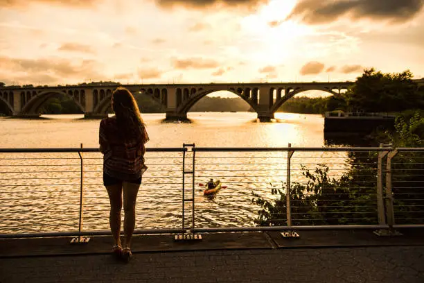 Photo of Back of young woman looking over potomac river with Francis Scott Key Bridge during sunset