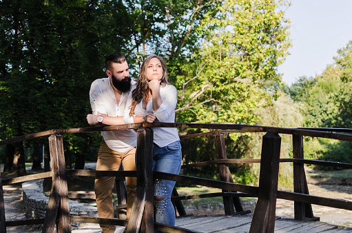 hipster man with big beard standing on wooden bridge and looking his depressed and sad woman, problems and conflicts in relationship or marriage, talking and dealing with problems, copy space