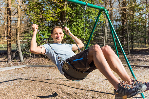 Young happy man on swing in playground smiling