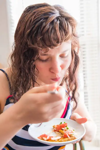 Closeup portrait of young woman eating and chewing healthy onion appetizer on chia flatbread toast salad with fork