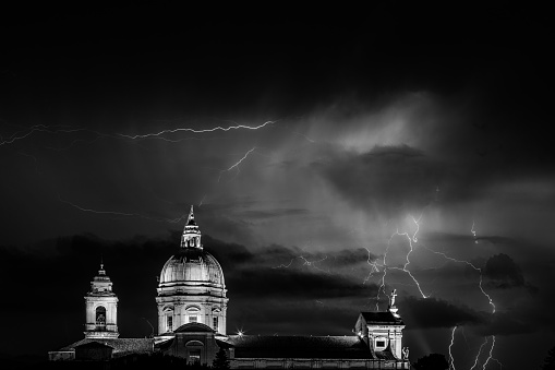 View of papal Santa Maria degli Angeli church (Assisi) with lightnings and thunderstorms striking above and near it, with a moody sky