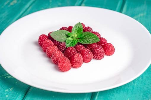 Fresh raspberries lying on a white plate on a white background