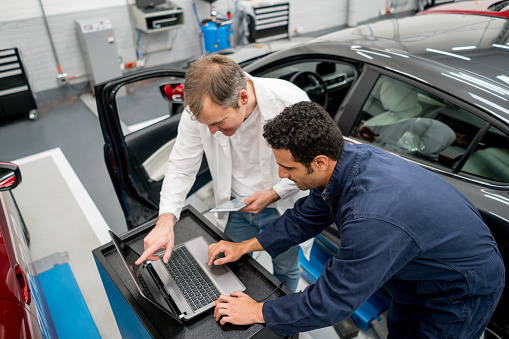 Team of mechanics working together at an auto repair shop using a computer to fix a car