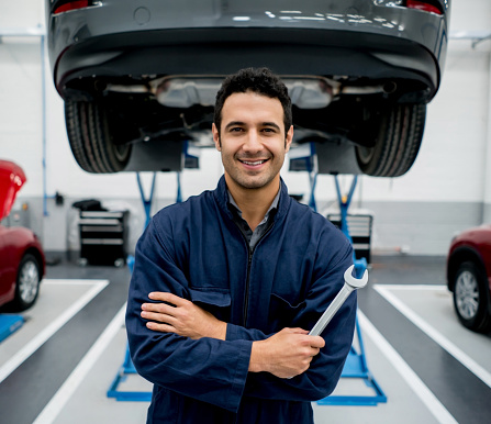 Portrait of a mechanic fixing cars at an auto repair shop holding a wrench and looking at the camera smiling